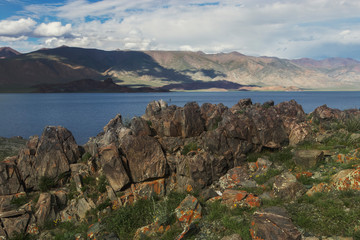 Sharp gray stones are covered with moss on the lake in Mongolia. Landscape with clouds, mountains on a sunny summer day. Traveling around the world.