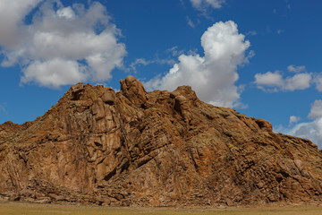 A high wall of yellow stones against a bright blue sky with white clouds. Traveling the steppes of Mongolia on a sunny summer day.