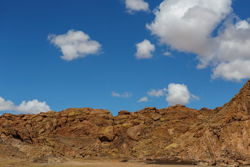 A high wall of yellow stones against a bright blue sky with white clouds. Traveling the steppes of Mongolia on a sunny summer day.