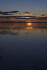 The setting sun and sky with fluffy clouds are reflected in the calm water of the lake. Traveled photo in Mongolia.