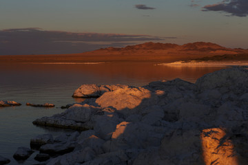 Large sharp stones lie in the lake and are illuminated by the orange light of the setting sun. Bright blue stars on a blue sky with clouds. Traveled photo in Mongolia. 