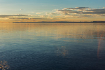 The smooth calm surface of the lake is lit by the light of the setting sun. The sky in orange tones is reflected in the water of the lake. Traveled photo in Mongolia.
