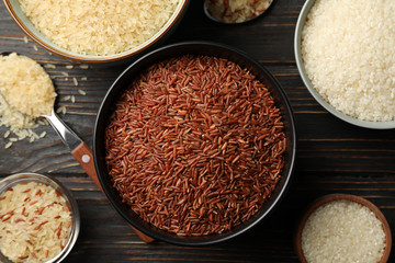 Bowls with different rice and spoons on wooden background, top view