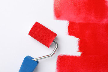 Roller and red paint strokes on white background, top view