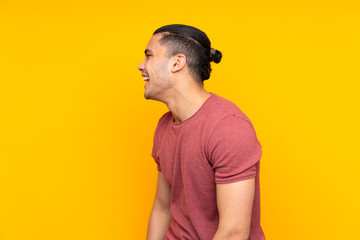 Asian handsome man isolated on yellow background whispering something with surprise gesture while looking to the side