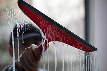 Window cleaner using a red squeegee to wash a window