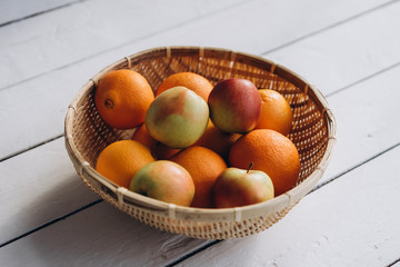  fresh fruits (apples and oranges) in a straw plate on a white wooden background close-up