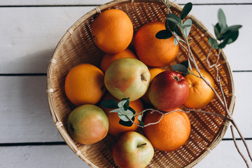  fresh fruits (apples and oranges) in a straw plate on a white wooden background close-up