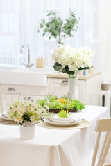 Served dining table with a white tablecloth, flowers, glasses and plates. sink by the window..