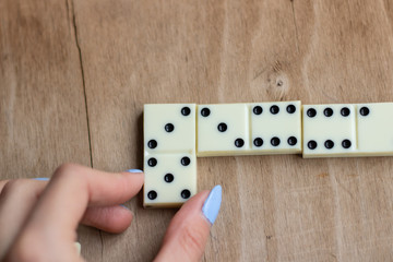 Play dominoes. Female hand puts domino bone on a brown table. 
