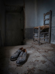 Silla y zapatos viejos en habitación de casa abandonada.
