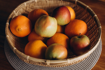  fresh fruits (apples and oranges) in a straw plate on a wooden table close-up