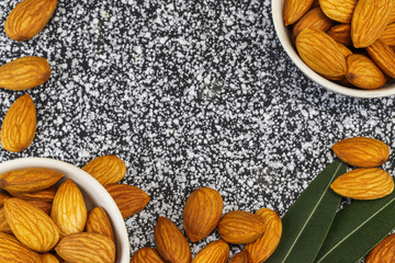 Almonds in two white bowls and on a black and white marble surface