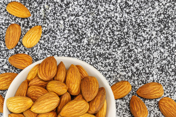 Almond nuts in a white bowl and on a black-white marble surface