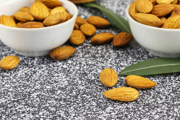 Two white bowls with almonds stand on a black and white marble surface