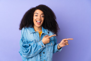 Young african american woman isolated on purple background surprised and pointing side