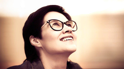 A beautiful dark-haired young woman with glasses smiles and looks up dreamily. Toning. Copy space