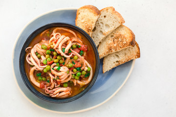 Squid with tomato and peas, served with crusty bread. Italian  cuisine. Homemade. Top view.