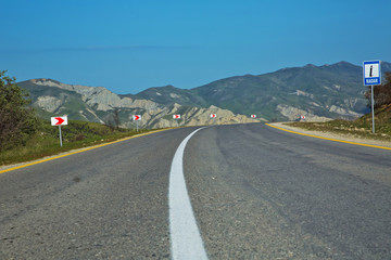 Winding country road in mountains . Asphalt road in the mountains with soft sky on the background. yellow and white line . Mountain road in poor condition .