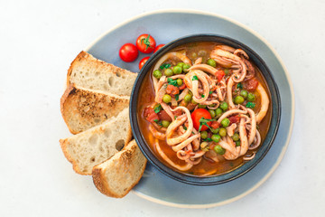Squid with tomato and peas, served with crusty bread. Italian  cuisine. Homemade. Top view.