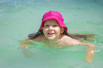 Little girl happily splashes in the water on a sunny day.