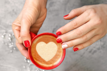Cup of coffee in female hands, heart manicure for Valentine's Day.