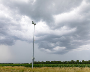 Severe weather alert and tornado warning siren along rural road with dark storm clouds and rain in background