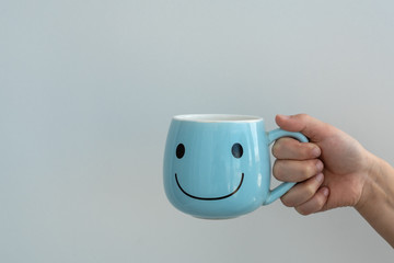kids hand holds big blue cup for tea or coffee with sign of big smile on it on white background, lots space for text, good morning and happy beginning of day concept