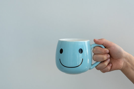 kids hand holds big blue cup for tea or coffee with sign of big smile on it on white background, lots space for text, good morning and happy beginning of day concept