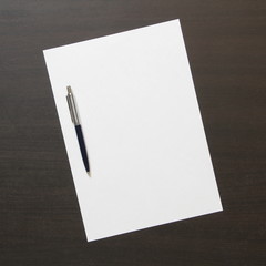 Template of white paper with pen on dark wenge color wooden background.