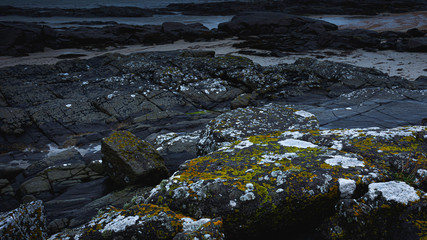 Fototapeta na wymiar Sanna beach on west coast of Scotland on gloomy day.Black, volcanic mossy basalt rocks on diverse Scottish coastline.Dark seascape scene with atmospheric mood and blue tones.Dramatic coastal landscape