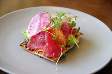 A creative spicy appetizer with raw tuna fish, oranges, avocado, a slice o radish and mustard seeds on a crisp