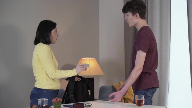 Side view of Caucasian mother and son quarreling at home. Woman showing condom found in boy's backpack, teenager justifies himself. Problem, family, conflict, worry.