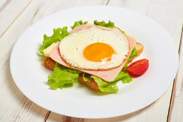 Toast with ham, egg and tomato on a plate on a light wooden background.