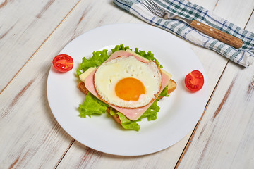 Toast with ham, egg and tomato on a plate on a light wooden background.