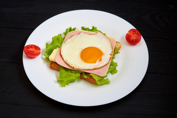 Toast with ham, egg and tomato on a plate on a black background.