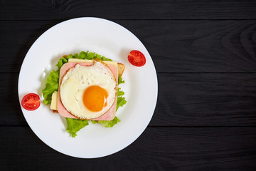 Toast with ham, egg and tomato on a plate on a black background.