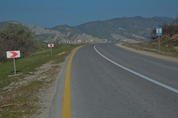 Fototapeta premium Winding country road in mountains . Asphalt road in the mountains with soft sky on the background. yellow and white line . Mountain road in poor condition .