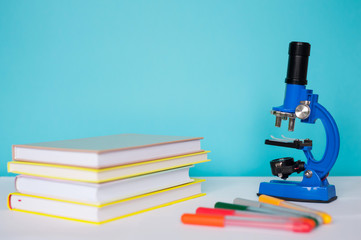 Blue microscope with books on a white table. The concept of schooling, research, discovery and creativity.