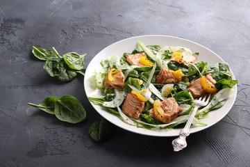 Leafy salad with red fried fish and orange on a white plate with a fork on a grey background. Background image, copy space