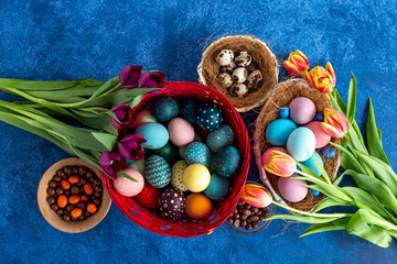 Obraz na płótnie Canvas Colorful Easter eggs in nest and tulips on deep blue background. Easter holiday decorations , Easter concept background.