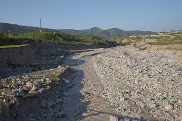 Stony river, high green mountains on the background. Rocks on river bed .The wild river stream has been working on stones for many years . Limestone riverbank. Running water in the river .