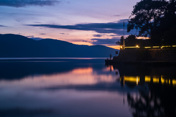 Mountains, rays and fishing man reflected in the sea at sunset. Tulle appearance at sea. Photographed with long exposure.