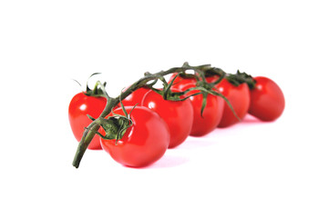 a branch of red cherry tomatoes sharp in front and blurred from behind on a white background