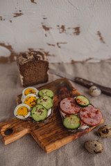 Set of sandwiches with rye bread, egg, ham, cucumber, cream cheese, seeds and spices on a wooden board. Rustic breakfast.