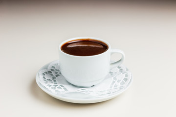 A small white cup of dark hot chocolate on a white saucer and a napkin