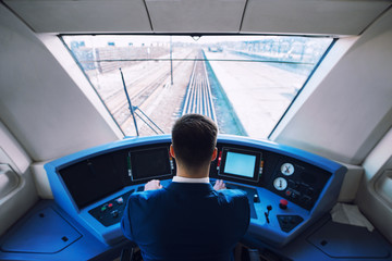 Shot of train cockpit interior with driver sitting and driving train. - obrazy, fototapety, plakaty