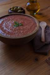 Bowl of Andalusian gazpacho with peppermint leaves with a rustic background with a wooden spoon