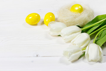 Fototapeta na wymiar Easter scene with yellow eggs in nest, and white tulips bouquet, flat lay on white wooden background