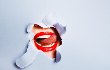 The Smile of a beautiful girl, with red lips through torn paper. Fashion and medical concept with dental hygiene